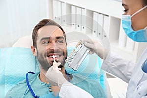 Dentist matching young man`s teeth color with palette