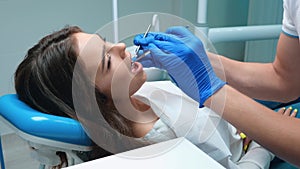 Dentist in medical blue gloves takes instruments and starts to cure patient woman`s teeth using dental mirror and dam