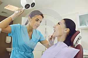 Dentist in medical uniform directing light to woman patients mouth for examination