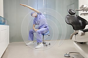 Dentist on mobile dental saddle stretching arm and back
