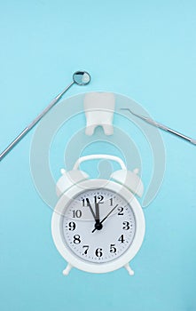 Dentist office tools for teeth care, tooth model molar and white alarmclock at blue background, top view, close up. Teeth care and