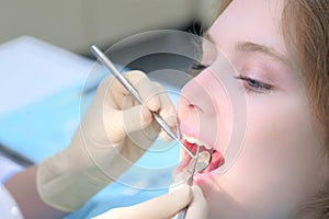 Dentist orthodontist examines girl`s teeth using dental tools needle and mirror.
