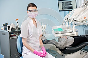Dentist with patient in the dental office. Doctor wearing glasses, mask, white uniform and pink gloves photo