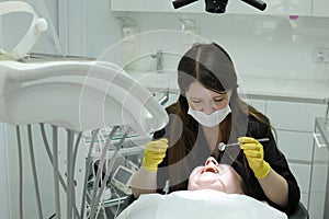 Dentist and patient in dentist office a dentist in black clothes and yellow gloves with a mirror and tools in his