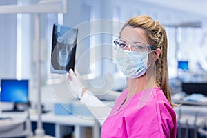 Dentist in pink scrubs holding an x-ray and looking at camera