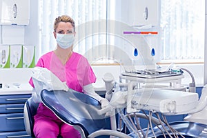 Dentist in pink scrubs looking at camera beside chair