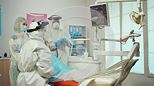 Dentist in ppe suit pointing on digital dental monitor explaining x-ray to mother