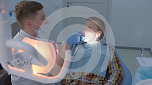 Dentist rinses boy`s mouth water holding saliva ejector during hygiene cleaning.