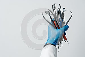 The dentist's hand in a blue glove holds bunch of dental instruments, dental mirror, tweezers, probe hooks.