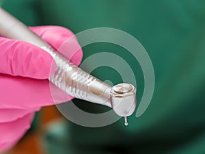 Dentist's hand in latex examination glove with dental handpiece.