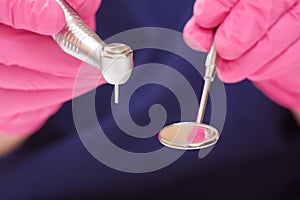 Dentist`s hands in glove with dental handpiece and mouth mirror