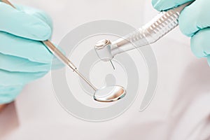 Dentist`s hands in gloves with dental handpiece and mouth mirror