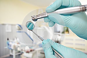 Dentist& x27;s hands in gloves with dental handpiece and mouth mirror.