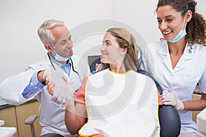Dentist shaking hands with his patient in the chair beside assistant