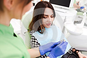 Dentist shows crown samples to his patient. Woman at the dentist`s appointment chooses the tone of veneers