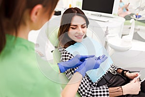 Dentist shows crown samples to his patient. Woman at the dentist`s appointment chooses the tone of veneers