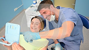 Dentist shows patient the results of treatment with a mirror, examinating teeth with dental equipment in dental office