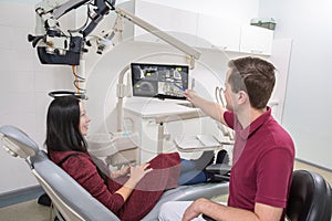 Dentist shows a patient x-ray of teeth. dental clinic. The patient is sitting in a chair. the dentist points the handle on the pic