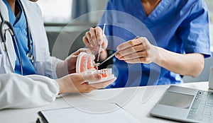 Dentist sitting at table with jaw samples tooth model and working with tablet and laptop in dental office professional dental