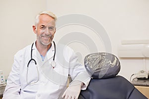 Dentist smiling at camera beside chair