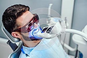 Dentist starting teeth whitening procedure with young man photo