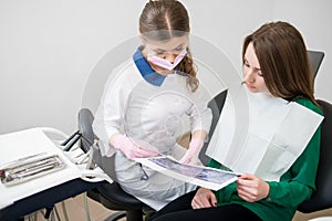 Dentist talking with female patient in dental clinic and preparing for treatment. Examining x-ray image. Dentistry