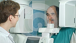Dentist talking to a senior patient before examination by using panoramic and cephalometric X-Ray scanner photo