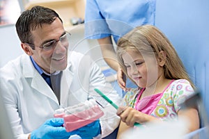 Dentist teaches girl properly brushing on model of teeth photo