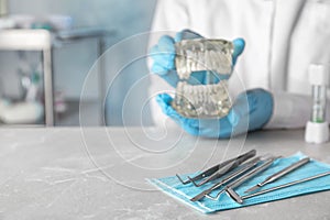 Dentist tools and blurred doctor with typodont teeth at table