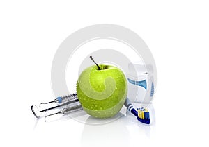 Dentist tools and fresh green apple with water drops isolated on white background in dental office. Dental care concept.