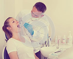 Dentist is treating female patient which is sitting in dental ch