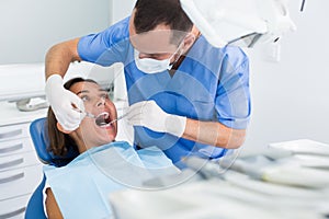 Dentist is treating female patient which is sitting in dental chair