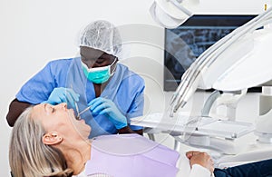 Dentist is treating female patient which is sitting in dental chair in clinic