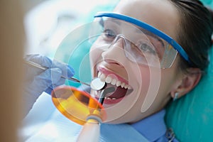 Dentist treating teeth to woman patient using curing light and dental instruments
