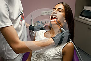 Dentist treats teeth of young woman using mouth dilator. Close u