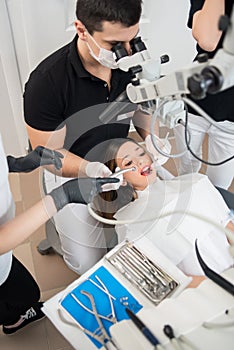 Dentist and two female assistants treating patient teeth with dental tools at dental clinic office. Dental equipment