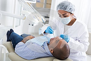 Dentist in uniform is examinating man on chair