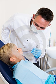 Dentist in uniform is examinating young boy