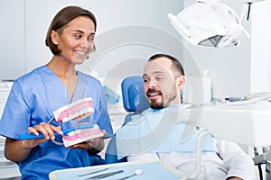 Dentist in uniform with maket of jaw is telling about healthcare