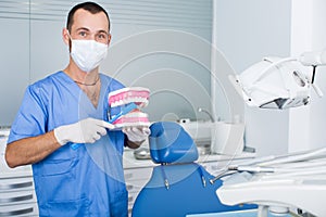 Dentist in uniform with maket of jaw is telling about healthcare