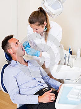 Dentist in uniform is taking visional inspection of an adult patiant on the chair