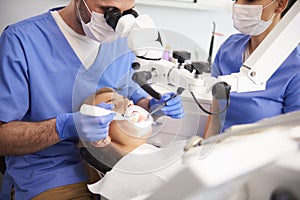 Dentist using dental microscope and examining woman`s teeth