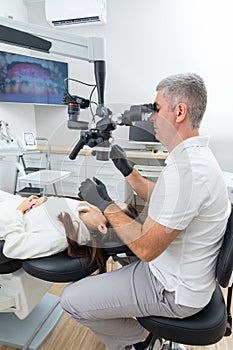 Dentist using dental microscope treating patient dental clinic office. Medicine, dentistry and health care concept