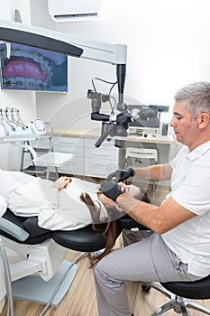 Dentist using dental microscope treating patient dental clinic office. Medicine, dentistry and health care concept