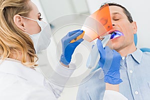 Dentist using uv lamp to treat patient teeth in modern