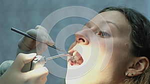 Dentist is washing his teeth with a mirror to a beautiful European woman. Visit to the dentist