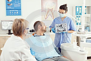 Dentist woman in dental office discussing with sick man while nurse showing tooth x-ray