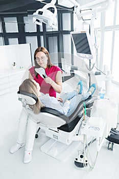 Dentist woman doctor talking to a young patient sitting on the dentist chair in a medical office. The first conversation