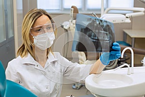 Dentist women in dental office stares intently at x-ray image of jaw