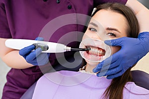 Dentist working with dental polymerization UV lamp in oral cavity for beautiful female patient